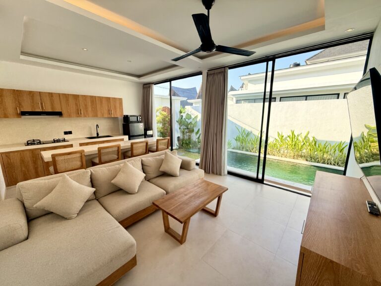 Open-plan living room with sofa, coffee table and kitchen bar, opening onto the pool