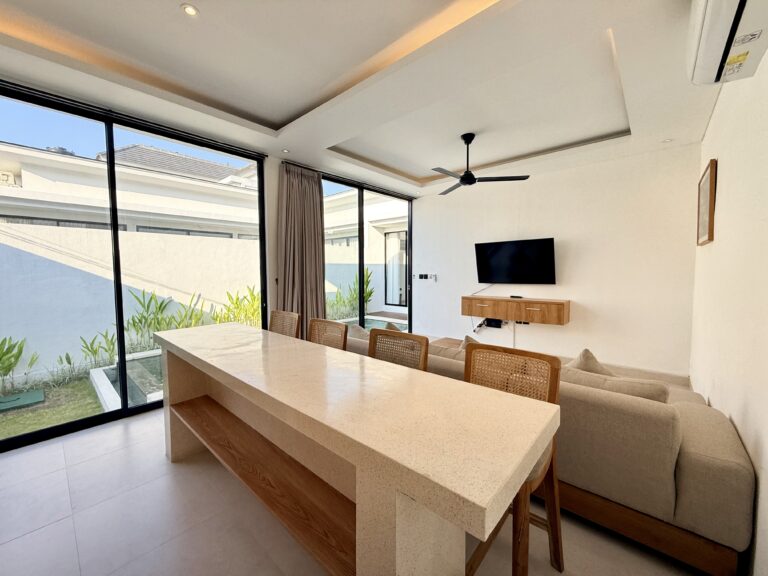 Long dining table with rattan chairs beside glass walls and a garden view